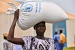 A closeup of a woman with a patterned brown and white shirt balancing a big white bag of WFP food on her head. Photo: WFP/Michael Tewelde